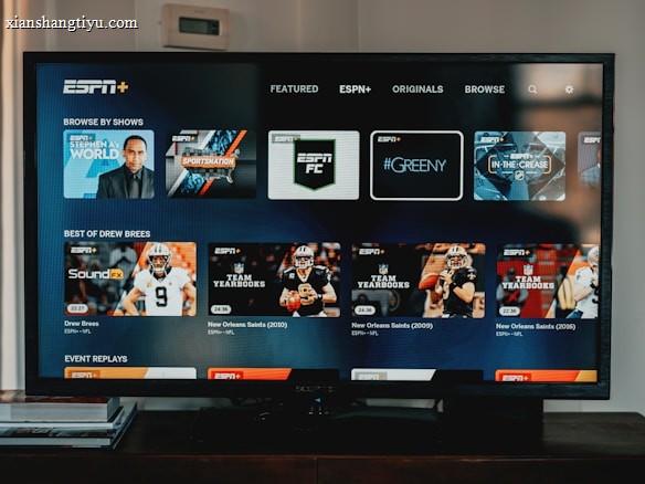A television screen displaying the ESPN+ streaming interface with various sports-related shows and categories. The screen includes sections such as 'Browse by Shows' and 'Best of Drew Brees' with thumbnails of sports programs featuring athletes in action and analysts.